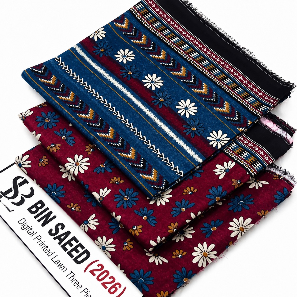 Three folded fabric or textile samples with printed patterns are stacked on a white background. The top sample is dark blue with geometric stripes and white floral motifs; the middle sample is burgundy with white and blue flowers; the bottom sample is dark red with white and blue flowers.