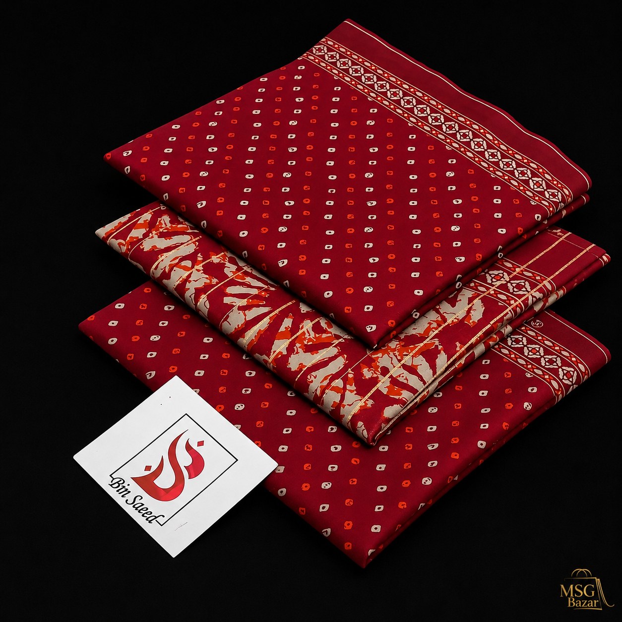 Three folded red patterned fabric pieces stacked on a black background, with a white tag reading '100% Silk' and a small 'MSG Bezar' logo in the bottom right corner.
