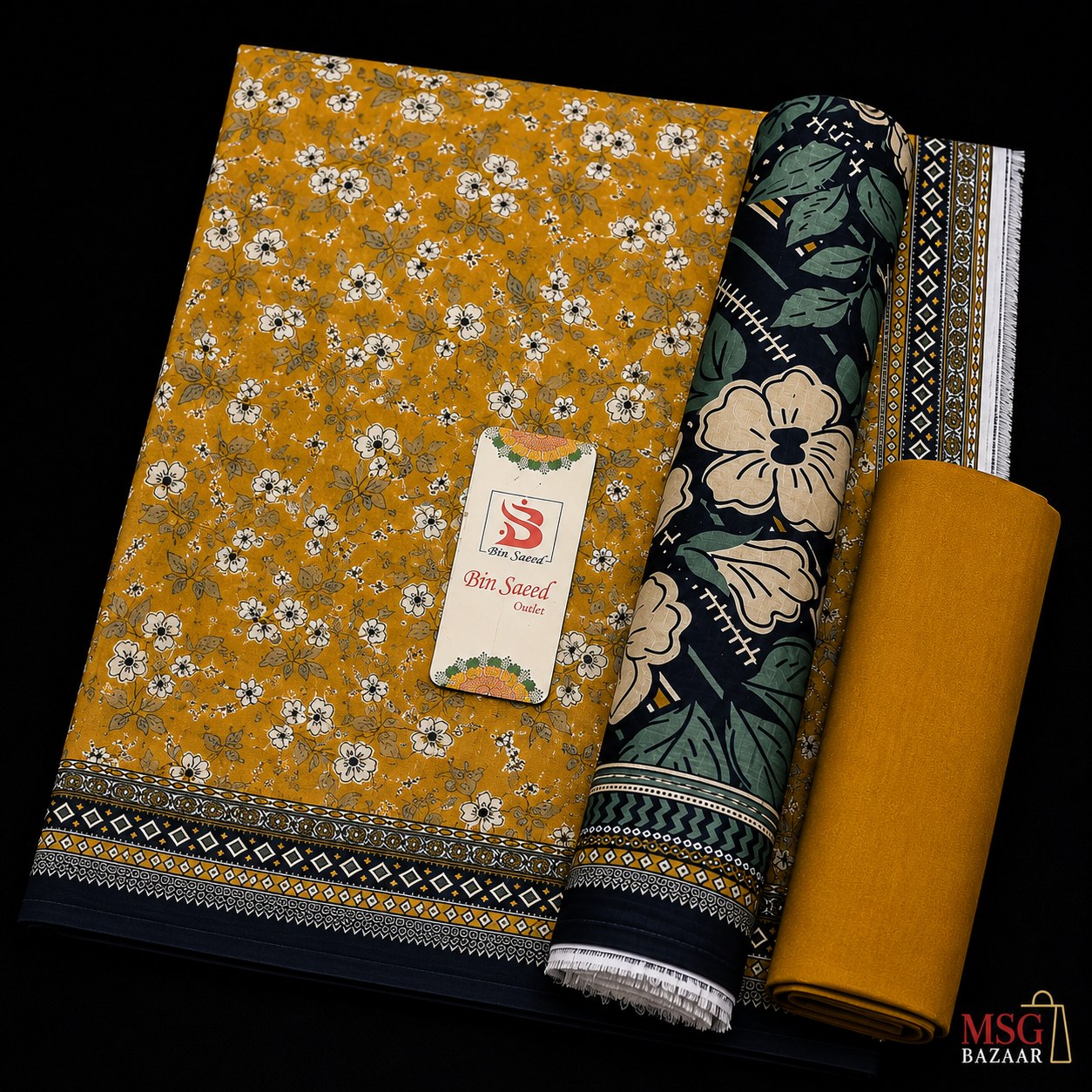 A folded and rolled fabric set on a black background, featuring a mustard yellow base with a white and green floral print, a dark green floral panel with cream flowers and leafy motifs, and a solid mustard yellow fabric roll. A paper tag reading '9th Sense Fabrics' is attached to the main fabric.