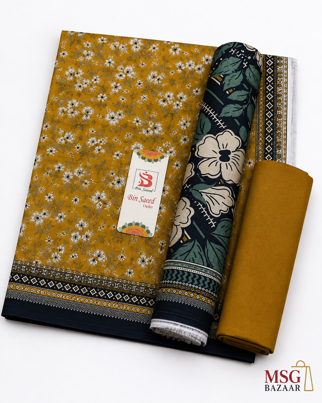 A folded and rolled piece of printed fabric set on a white background, with a visible tag reading 'Saffron' and a 'MSG BAZAAR' watermark in the corner. The fabric features a mustard yellow base with a white and green floral print, a dark navy border with floral motifs, and a solid mustard yellow rolled section.