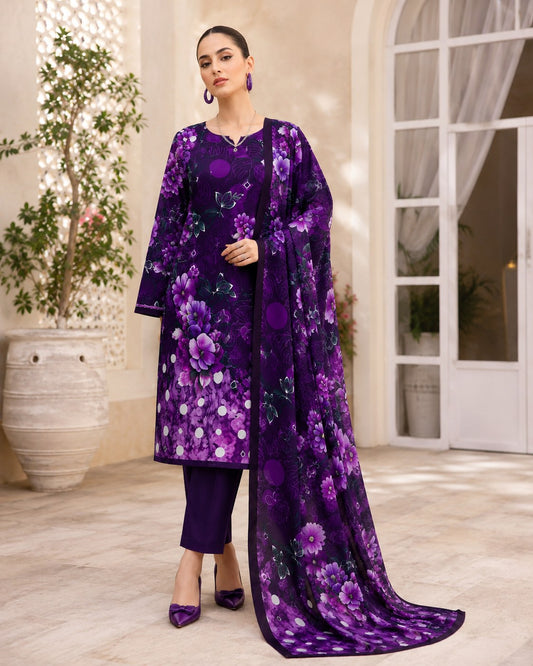 A woman models a traditional three-piece purple floral salwar kameez suit with matching pants and dupatta in an elegant indoor courtyard setting.