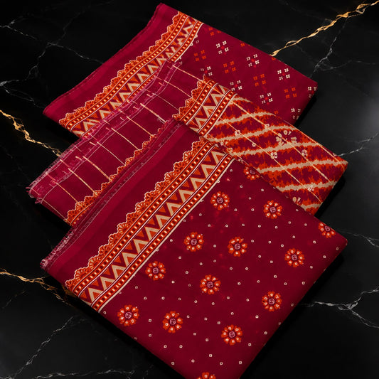 Three folded pieces of deep red fabric with orange and white traditional patterns and borders, arranged diagonally on a black marble surface with gold veins.