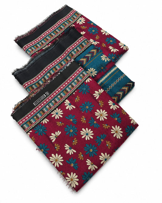 Three folded patterned scarves stacked diagonally on a white background. The top scarf is black with colorful geometric borders.