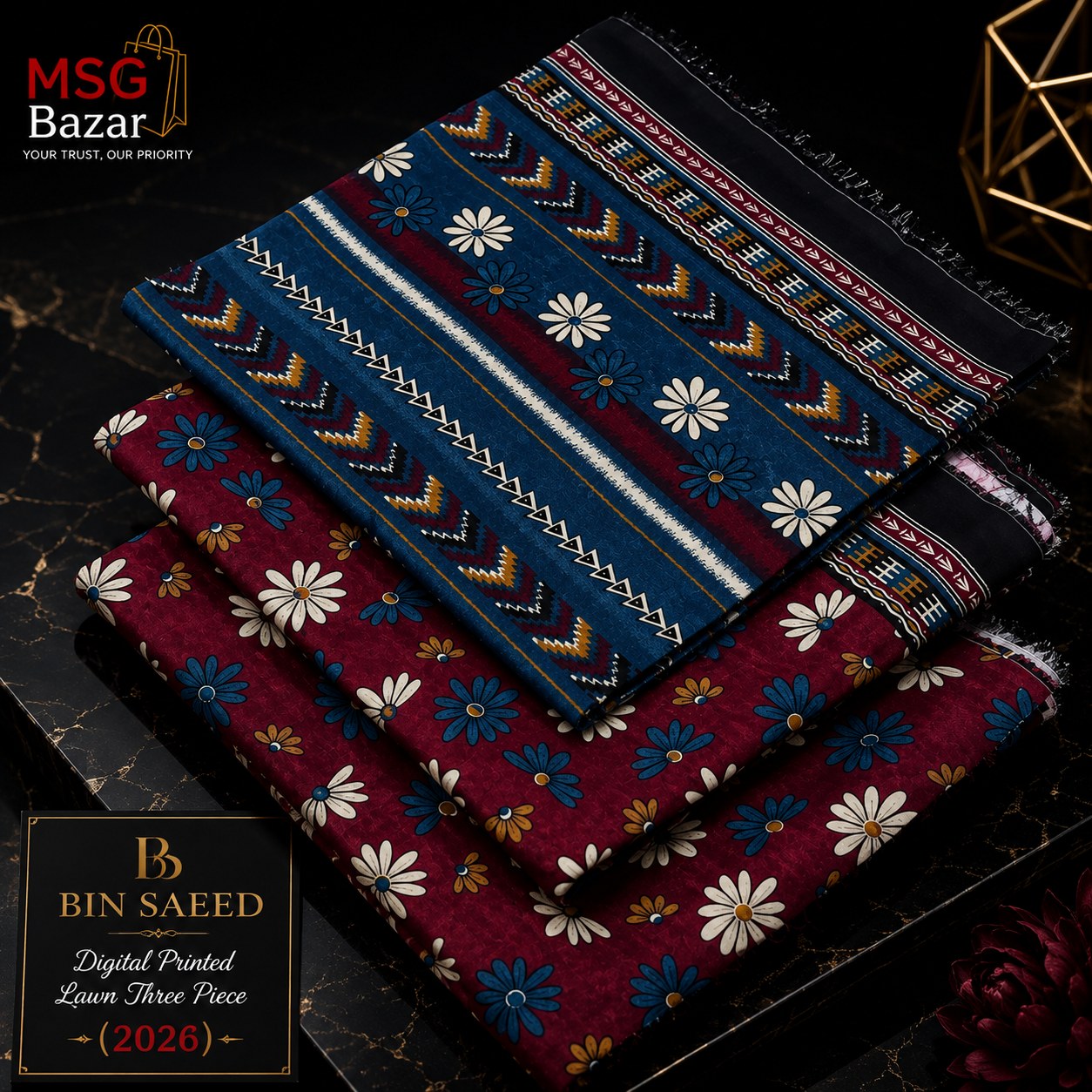 Three folded patterned fabric pieces stacked on a dark marble surface, with a black branded box at lower left. The top fabric is dark blue with white, yellow, and red geometric motifs; the middle is deep red with white and blue floral prints; the bottom is black with white and red geometric motifs.