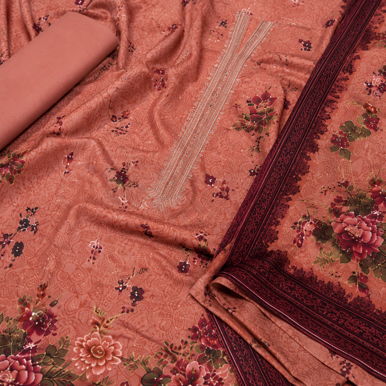 A peach-colored fabric set with a floral print, featuring a matching rolled fabric piece, a main draped cloth with embroidered neckline details, and a decorative border.