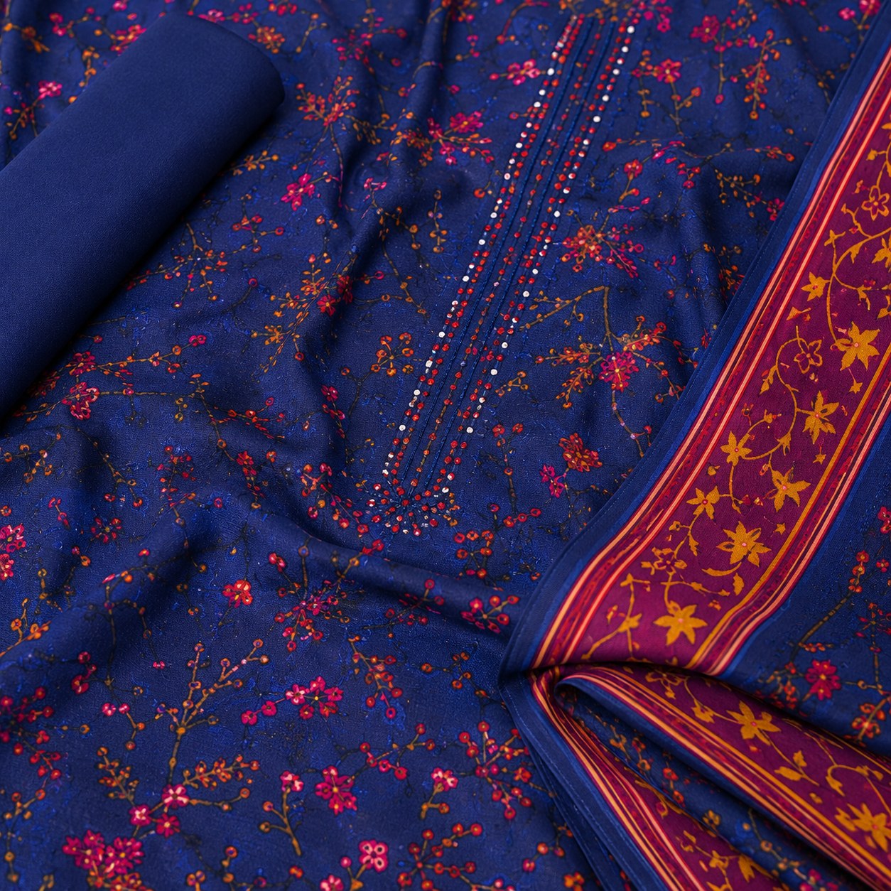 A close-up of a navy blue fabric with a dense red and orange floral print, featuring a decorative border with yellow floral motifs and red stripes.