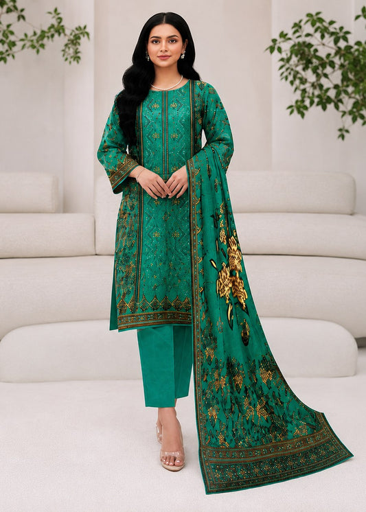 A woman models a traditional three-piece salwar kameez suit in emerald green with gold and yellow floral embroidery, featuring a long tunic, matching trousers, and a draped dupatta, posed in front of a modern white curved sofa.