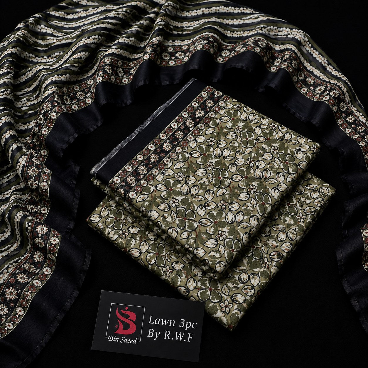 A folded fabric set with an olive green and beige floral block print, a black border, and a matching patterned dupatta draped around it on a black background. A black label at the bottom reads 'Bin Saved By R.