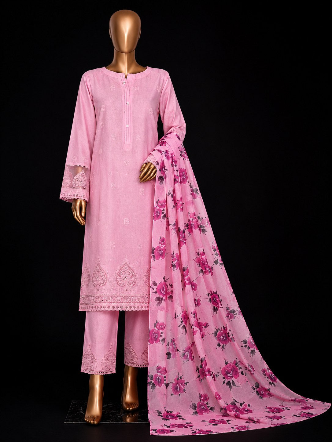 A pink traditional three-piece outfit displayed on a gold mannequin against a black background, featuring a long-sleeve embroidered kurta, matching trousers, and a floral printed dupatta.