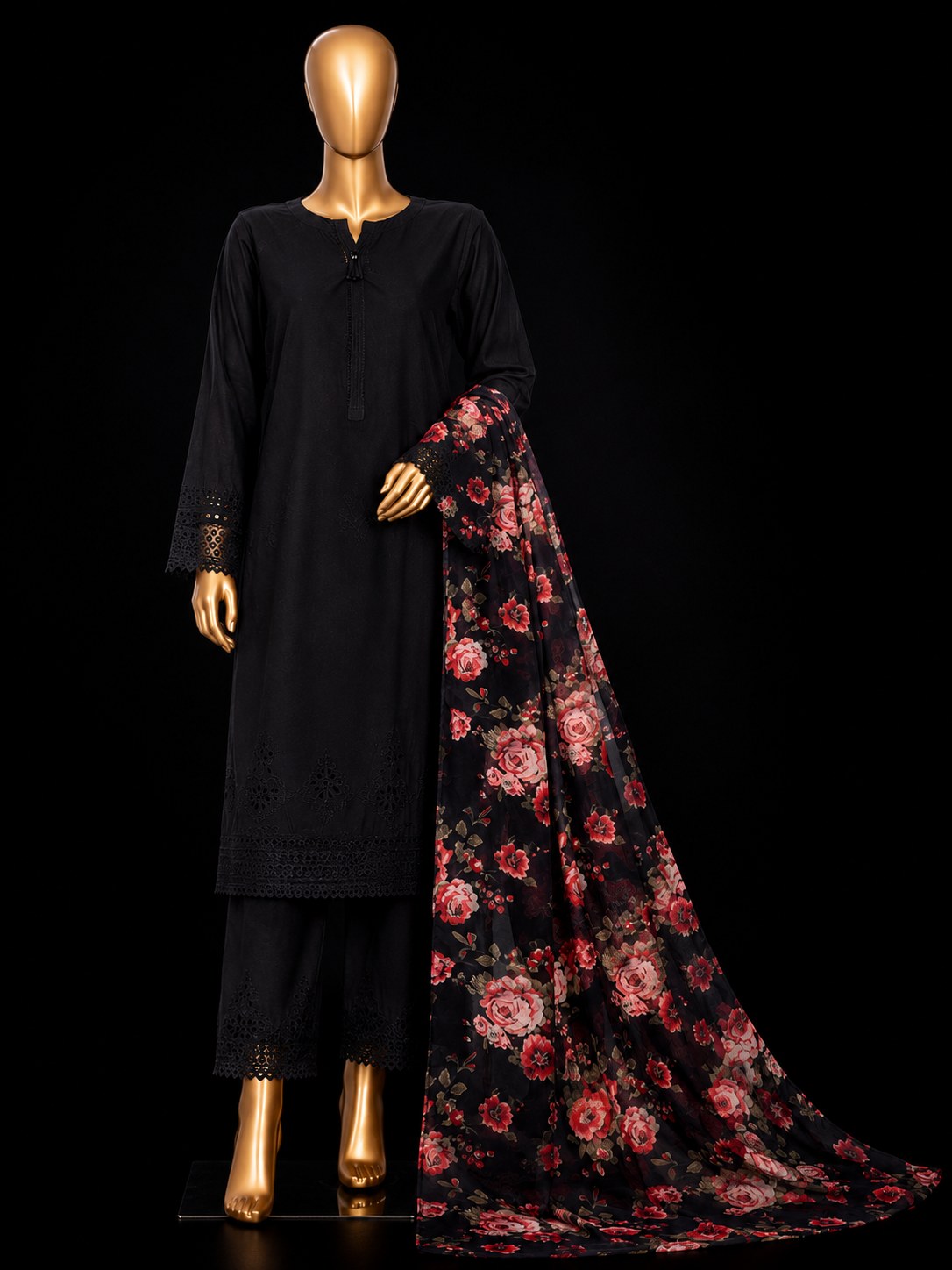 A black women's traditional outfit displayed on a gold mannequin against a black background, featuring a long-sleeve embroidered kurta, matching pants, and a sheer black dupatta with a red and pink floral pattern.