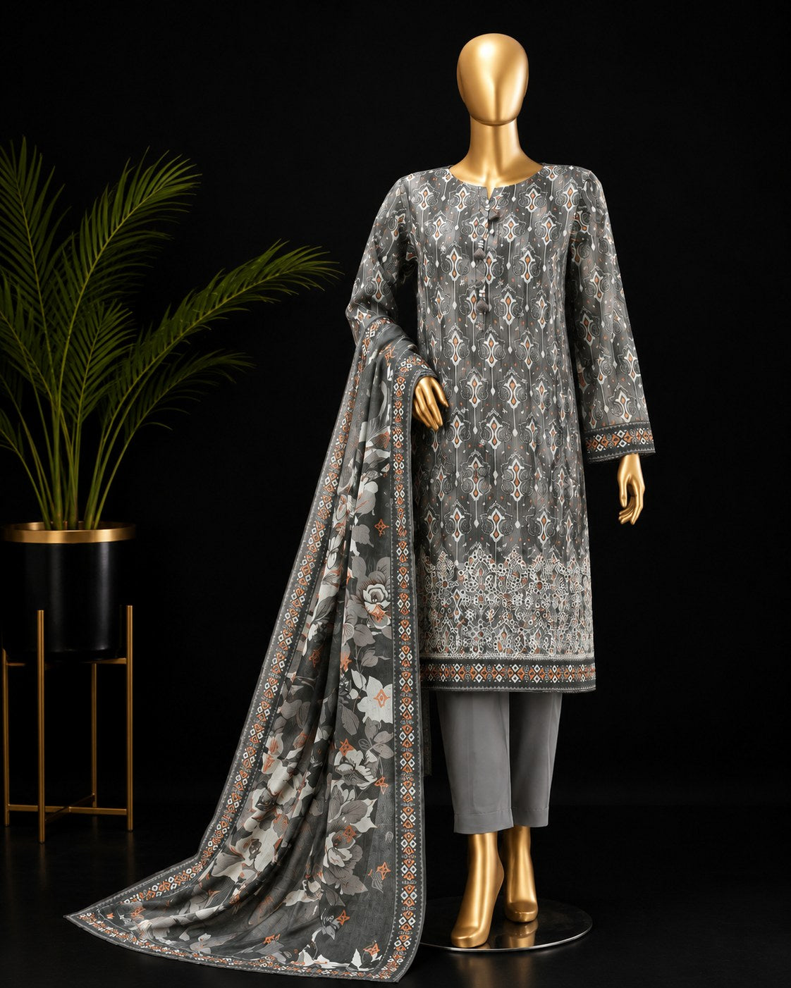 A three-piece men's traditional outfit displayed on a gold mannequin against a black background, featuring a gray kurta with intricate white and orange geometric patterns, matching gray trousers, and a coordinating dupatta with floral motifs.