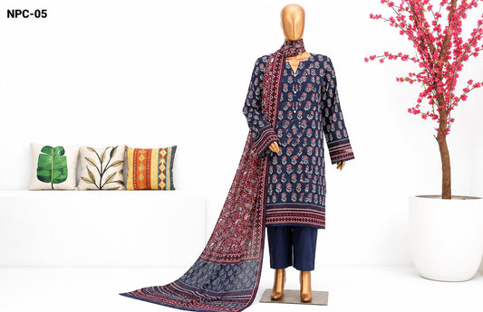 A three-piece Indian ethnic suit set displayed on a mannequin, featuring a navy blue kurta with red and gold floral prints, matching navy pants, and a coordinating dupatta. The set is styled in a clean studio setting with decorative pillows and a potted pink tree.