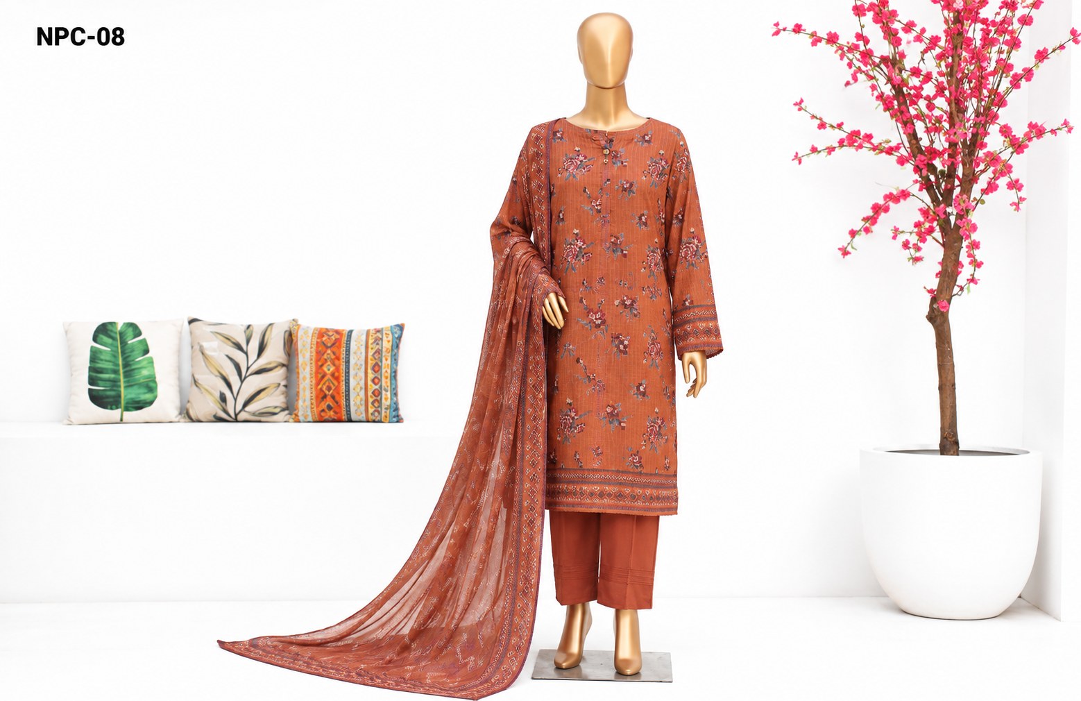 A 3-piece unstitched salwar kameez suit set in rust orange, displayed on a mannequin. The set includes a long-sleeved kurta with floral embroidery, matching trousers, and a dupatta.