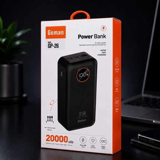 Geman Power Bank GP-26 retail packaging box shown on a dark tabletop with a blurred laptop and plant in the background. The box is white and orange with a large photo of the black power bank on the front.